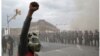 A demonstrator raises his fist on April 27, 2015, in front of police and a burning building during unrest following Freddie Gray's funeral, top, and a man walking children across the same street on April 19, 2016, in Baltimore.