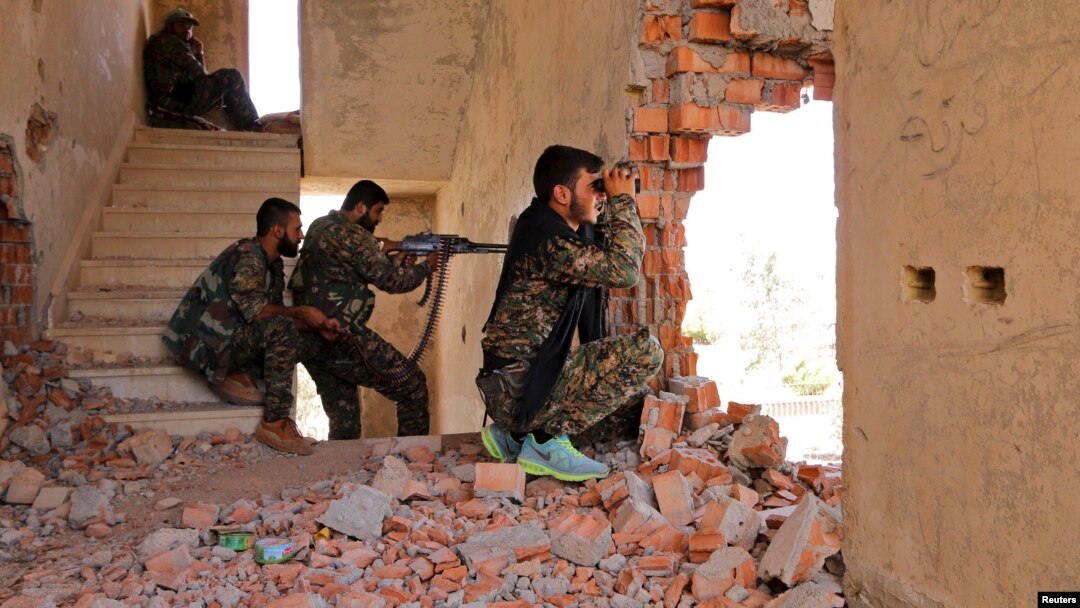 FILE - Kurdish People's Protection Units (YPG) fighters take up positions inside a damaged building in al-Vilat al-Homor neighborhood in Hasaka city, as they monitor the movements of Islamic State fighters.
