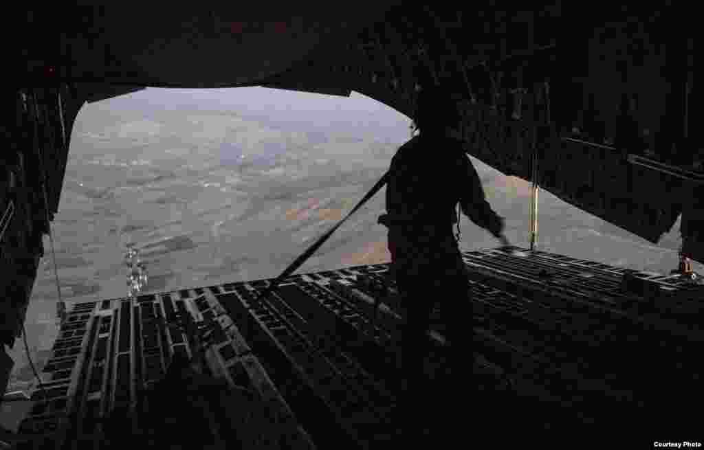 Tech. Sgt. Lynn Morelly, 816th Expeditionary Airlift Squadron, C-17 Globemaster III loadmaster, watches bundles of halal meals parachute to the ground during a humanitarian airdrop mission, over the vicinity of Sinjar, Iraq, Aug. 9, 2014. (U.S. Air Force)