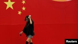 FILE - A woman wearing a mask walks past a wall painted with China's national flag in central Beijing.