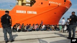 Para migran yang diselamatkan duduk berbaris setelah turun dari kapal kargo Norweia, Siem Pilot, di pelabuhan Reggio Calabria, Italia (8/8). (AP/Adriana Sapone)