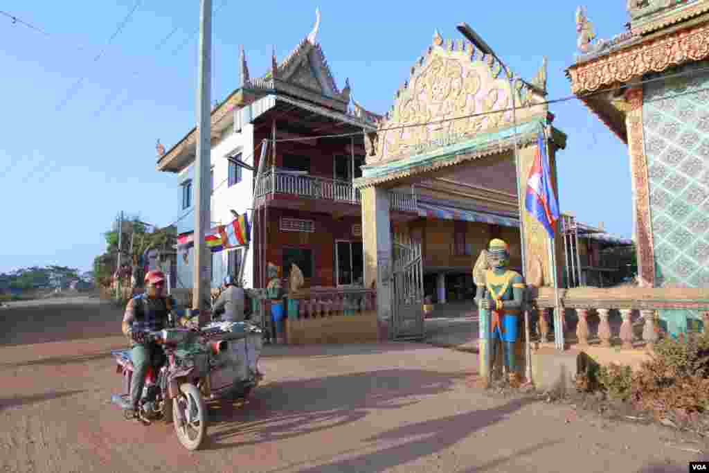 បុរស​ម្នាក់​ជិះ​ម៉ូតូ​លក់​ម្ហូប​របស់​គាត់​កាត់​មុខ​វត្ត​បំពេញ​កុសល (ហៅ​វត្តពាម) នៅ​ភូមិ​ពាម ក្នុង​ខេត្តកណ្ដាល​ ដែល​មាន​ការ​សង្ស័យ​ថា ​មាន​ឆ្លង​រាល​ដាល​មេរោគ​អេដស៍​ទ្រង់​ទ្រាយ​ធំ កាលពី​ថ្ងៃច័ន្ទ ទី២២ ខែ​កុម្ភៈ ឆ្នាំ២០១៦។ (រូបថត៖ អូន ឆេងប៉រ/VOA)