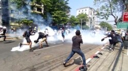 In this image from a video, anti-coup protesters run away from tear gas launched by security forces in Yangon, Myanmar, March 1, 2021. Defiant crowds returned to the streets of Myanmar's biggest city on Monday.
