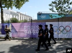 Seorang tentara dan polisi berpatroli di dekat spanduk Olimpiade Paris 2024 di Paris, sembilan hari menjelangg dimulainya Olimpiade Paris, Rabu, 17 Juli 2024. (Aurelien Morissard/AP)