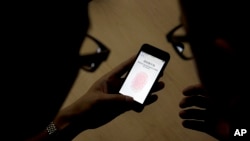 FILE - In this Sept. 11, 2013 photo, an Apple employee (r) instructs a journalist on the use of the fingerprint scanner technology built into the company's iPhone 5S during a media event in Beijing. Two U.S. senators are expected to introduce a bipartisan bill that would impose penalties on technology companies that refuse a court order to unlock smartphones.