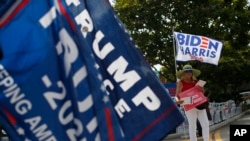 Para pendukung Presiden Donald Trump dan pendukung mantan wakil presiden Joe Biden melambaikan bendera di luar tempat pemungutan suara awal di West Palm Beach, Florida, Jumat, 30 Oktober 2020. (Foto: AP)