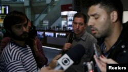 U.S. journalist Glenn Greenwald (C) looks on as his partner David Miranda (R) talks with the media after arriving at Rio de Janeiro's International Airport, Brazil, Aug. 19, 2013.