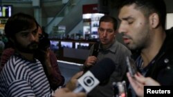 El periodista estadounidense Glenn Greenwald al centro en la foto observa a su pareja, David Miranda a la derecha en la foto, quien habla con los medios de prensa a su llegada a Río de Janeiro tras haber sido detenido en Londres.