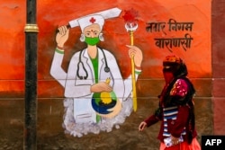 Seorang wanita dengan wajah tertutup kain berjalan melewati mural dinding yang mempromosikan kesadaran tentang penggunaan masker di Varanasi, India, 7 Januari 2025. (Foto: AFP)