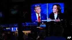 People watch TV screens showing the debate between Democratic presidential nominee Vice President Kamala Harris, right, and Republican presidential nominee former President Donald Trump at Sports Grill Kendall in Miami, Florida, Sept. 10, 2024.