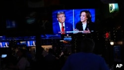 People watch TV screens showing the debate between Democratic presidential nominee Vice President Kamala Harris, right, and Republican presidential nominee former President Donald Trump at Sports Grill Kendall in Miami, Florida, Sept. 10, 2024. 