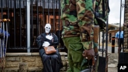 FILE - An armed police officer walks past an environmental protester wearing a skeleton costume as she demonstrates outside parliament against recent government plans to mine coal and open a coal-fired power plant, in downtown Nairobi, Kenya, June 5, 2018. 