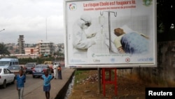 People walk past a billboard displaying a government message about Ebola that reads: "The risk of Ebola is still there. Let us apply the protective measures together", Abidjan, Ivory Coast, Sept.10, 2014.