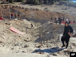 Seorang perempuan membawa barang bawaan menyeberang ke Suriah dengan berjalan kaki melewati kawah akibat serangan Israel yang memotong jalan antara Lebanon dan Suriah di penyeberangan Masnaa, Lebanon, Jumat, 4 Oktober 2024. (Foto: Samer Husseini/AP Photo)