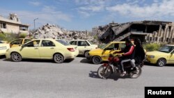 FILE - Men ride a motorbike past cars, in line at a gasoline station, waiting to fuel up, in Aleppo, Syria April 11, 2019.