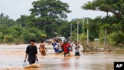 Sejumlah warga lokal berjalan melewati jalan yang tergenang banjir sambil membawa makanan di Naypyitaw, Myanmar, pada 14 September 2024. (Foto: AP/Aung Shine Oo)