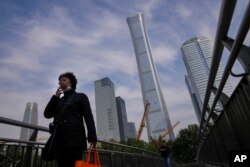 Seorang perempuan berjalan di dekat derek konstruksi dekat gedung pencakar langit di Kawasan Pusat Bisnis di Beijing, Senin, 18 Oktober 2021. (Foto: AP)