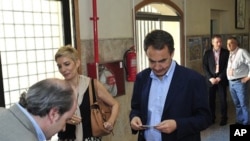 An official checks Spain's Prime Minister Jose Luis Rodriguez Zapatero's identification before voting, with his wife Sonsoles Espinosa at left, at a voting center in Madrid, May 22, 2011