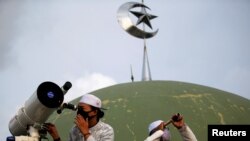 A boarding school student and an official use a telescope and a monocular to view the moon on the roof of Al Musariin mosque to mark the first day of Ramadan in Jakarta, Indonesia.