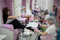 Nail technicians wearing face masks and gloves perform manicure and pedicure for their clients in a nail bar in Moscow, Russia, June 9, 2020.