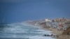 FILE - People walk along the beach next to a tent refugee camp for displaced Palestinians in Deir al-Balah, central Gaza Strip, Dec .30, 2024. 