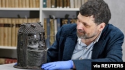 Neil Curtis, head of Museums and Special Collections is seen with one of the Benin bronze depicting the Oba of Benin at The Sir Duncan Rice Library, the University of Aberdeen, Scotland, March 17, 2021. (University of Aberdeen/Handout via Reuters)
