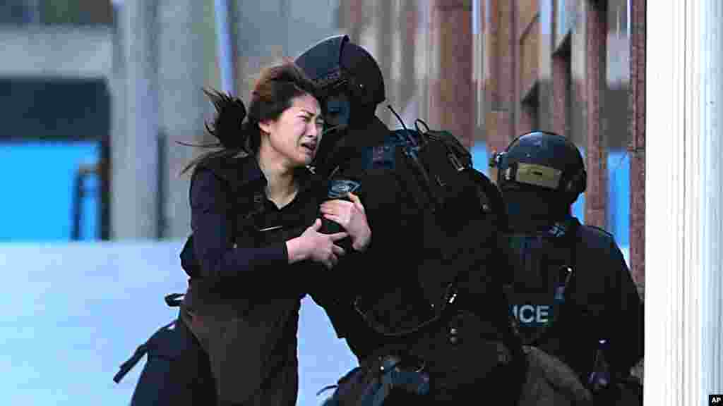 Un otage accourt vers des policiers armés de réponse tactiques pour la sécurité après avoir échappé d&rsquo;un café en état de siège à la place Martin, dans le quartier central des affaires de Sydney, en Australie, le lundi 15 décembre 2014.