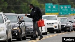 在北卡州達勒姆，一位男士提著汽油箱走過排在一處加油站外的長長的車隊。(2021年5月12日)