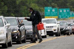 FILE - A man with a gas container greets a motorist waiting in a lengthy line to enter a gasoline station during a surge in the demand for fuel following the cyberattack that crippled the Colonial Pipeline, in Durham, North Carolina, May 12, 2021.