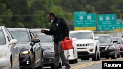 A man with a gas container is greeted by a motorist waiting in a lengthy line to enter a gasoline station during a surge in the demand for fuel following the cyberattack that crippled the Colonial Pipeline, in Durham, North Carolina, May 12, 2021.