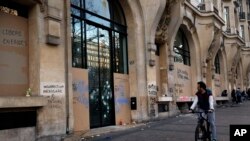 A man rides his bicycle past a damaged store after a yellow vests demonstration, March 16, 2019 in Paris. 