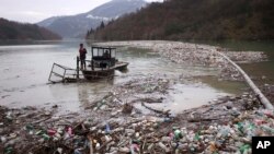FILE - Utility company workers push the waste to the shore of Lim river near Priboj, Serbia, Jan. 30, 2023.