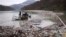 FILE - Utility company workers push the waste to the shore of Lim river near Priboj, Serbia, Jan. 30, 2023.