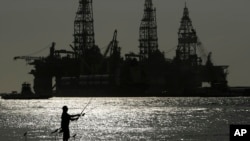 Seorang pria memancing di dekat platform pengeboran minyak yang berlabuh, di Port Aransas, Texas, 8 Mei 2022. (AP Photo/Eric Gay). 