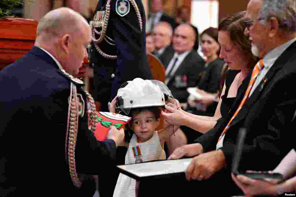 Charlotte O&#39;Dwyer, the daughter of Rural Fire Service volunteer Andrew O&#39;Dwyer, receives her father&#39;s helmet and a service medal by RFS Commissioner Shane Fitzsimmons during his funeral in Horsley Park, Sydney, Australia. 
