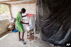 Mouhamed Sall, who is deaf, and known for his talent for drawing and manual activities, paints a small house he built in Pikine, Senegal, Monday, March 18, 2024. (AP Photo/Sylvain Cherkaoui)