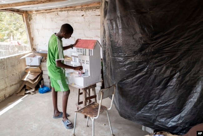 Mouhamed Sall, who is deaf, and known for his talent for drawing and manual activities, paints a small house he built in Pikine, Senegal, Monday, March 18, 2024. (AP Photo/Sylvain Cherkaoui)