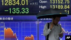 A man checks his mobile phone in front of the electronic stock board of a securities firm in Tokyo, June 2013.