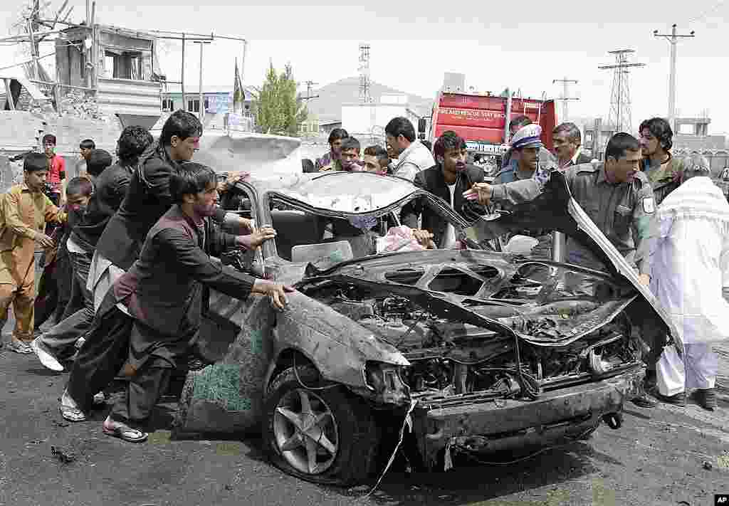 Warga Afghanistan mendorong kendaraan yang rusak dihantam bom di lokasi ledakan di Kabul (AP).