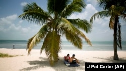 FILE - In this July 1, 2015 file photo, Marvin Hernandez, right, and Kelly Vera sit in the shade of a palm tree, in Key Biscayne, Florida.