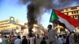 FILE - A Sudanese man wearing a face mask waves his country's national flag during protests in the capital, Khartoum, to mark the second anniversary of the start of a revolt that toppled the previous government, on Dec. 19, 2020. 