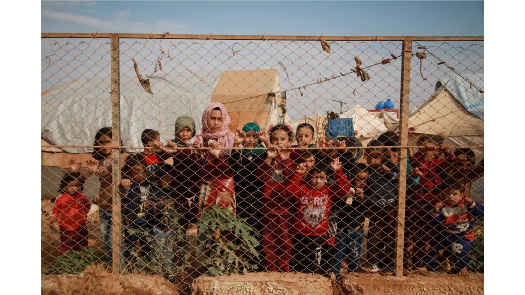 FILE - Displaced Syrian children stand behind a fence outside their tents in a camp set up near the village of Kafr Lusin, in Idlib's northern countryside, near the Syria-Turkey border, Oct. 22, 2019.