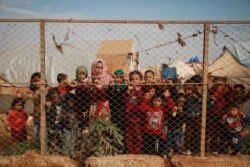 FILE - Displaced Syrian children stand behind a fence outside their tents in a camp set up near the village of Kafr Lusin, in Idlib's northern countryside, near the Syria-Turkey border, Oct. 22, 2019.