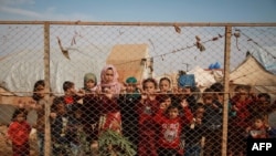 Displaced Syrian children stand behind a fence outside their tents in a camp set up near the village of Kafr Lusin, in Idlib's northern countryside, near the Syria-Turkey border, Oct. 22, 2019. 