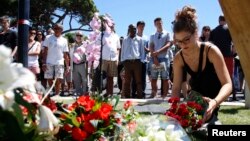 A woman places a bouquet of flowers as people pay tribute near the scene where a truck ran into a crowd at high speed killing scores and injuring more who were celebrating the Bastille Day national holiday, in Nice, France, July 15, 2016. 