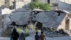 FILE - People walk near rubble of damaged buildings in the city of Idlib, Syria, May 27, 2019.