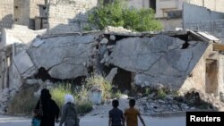 People walk near rubble of damaged buildings in the city of Idlib, Syria, May 27, 2019. 