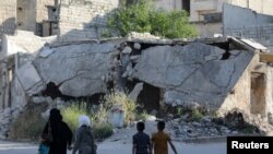 FILE - People walk near rubble of damaged buildings in the city of Idlib, Syria, May 27, 2019.