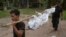 Workers carry a dead body in Songkhla province, southern Thailand, May 1, 2015. Police in Thailand found dozens of shallow graves Friday and at least one corpse in an isolated mountain shelter that is believed to be a trafficking camp for ethnic Rohingya Muslims fleeing Myanmar.