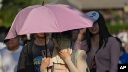 Una mujer cubierta con un paraguas camina entre la multitud en un día caluroso y soleado en Beijing, el domingo 16 de junio de 2024. Foto AP